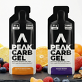 Two Peak Carb Gel packages with fruit and snacks in the background