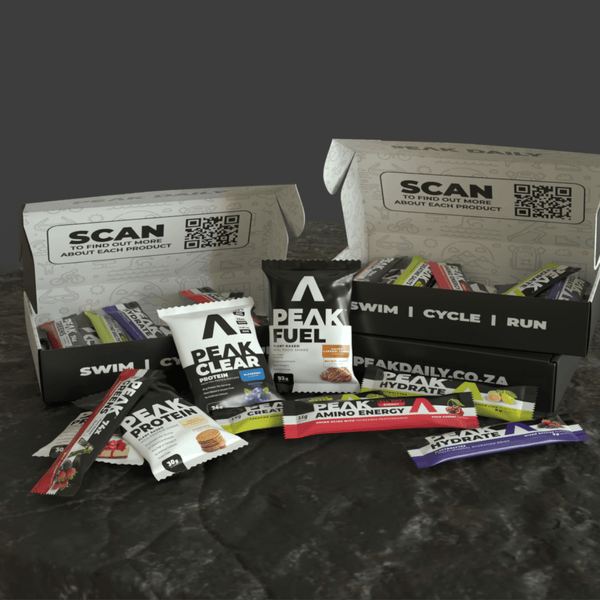 Assorted Peak Fuel products including bars and packets on a dark surface with branded boxes.